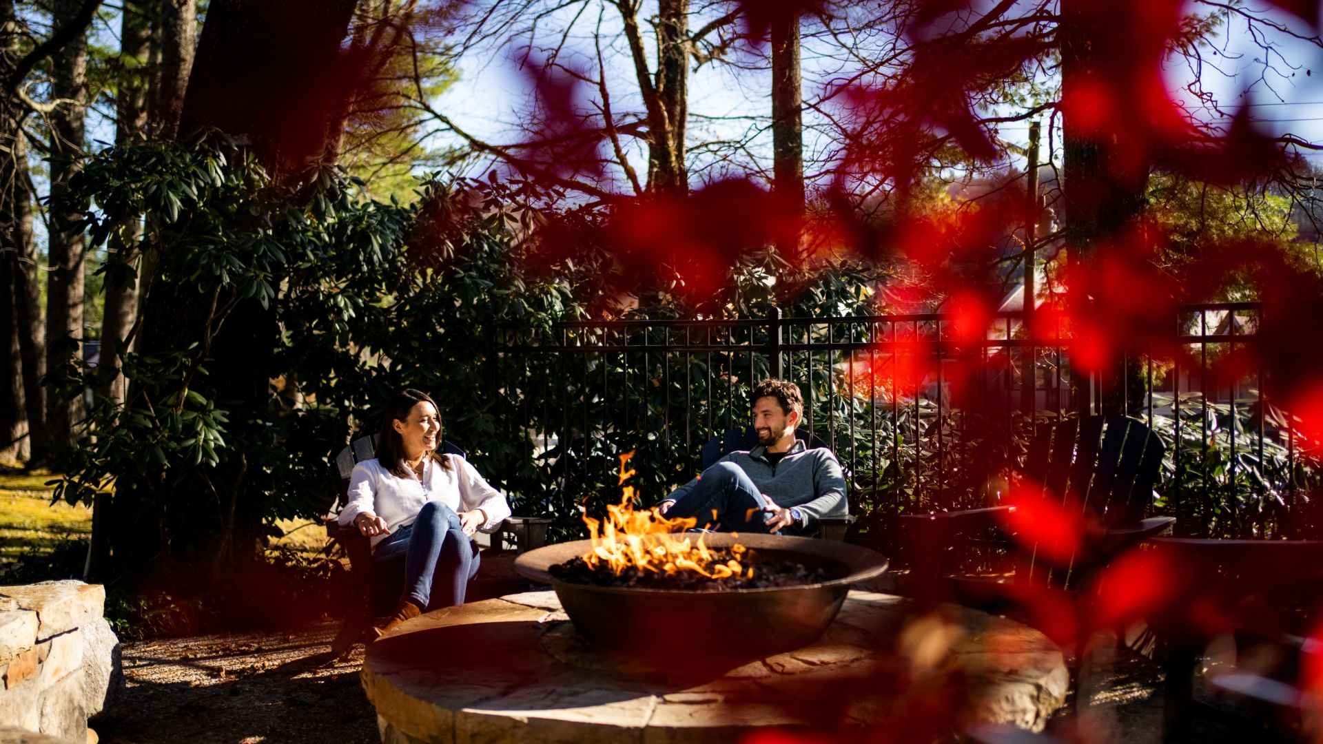 A Man And Woman Sitting At A Table With A Fire In A Fire Pit