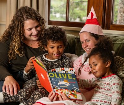 A Person And Two Children Sitting On A Couch With A Santa Hat